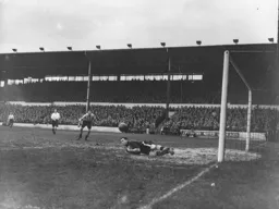 Reg Newton appears to fumble the ball as Bert Mitchell watches from a distance