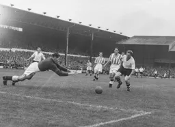 Ted Ditchburn comes out of his goal to dive at the feet of Peter MacEwan