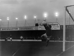 Cobblers goalkeeper Brian Caine makes a save under Luton's dim floodlights
